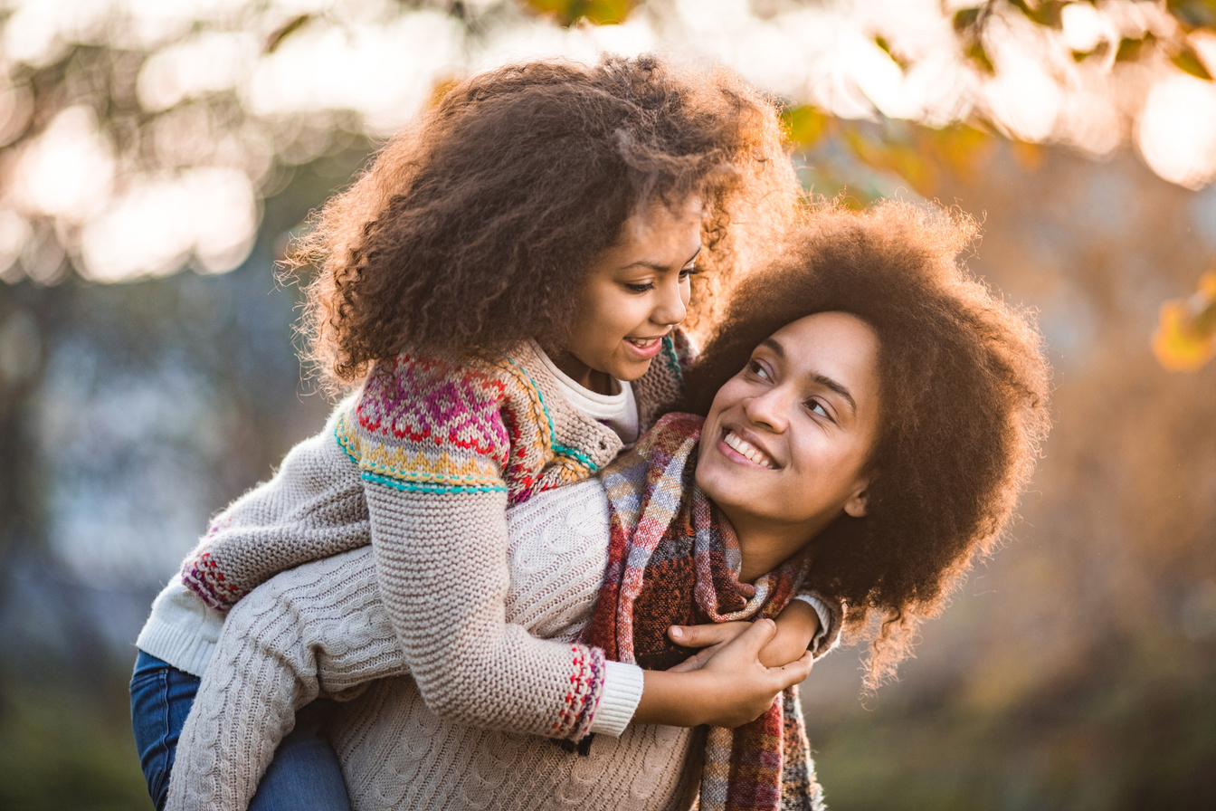 Happy black mother and daughter communicating while piggybacking in autumn day.